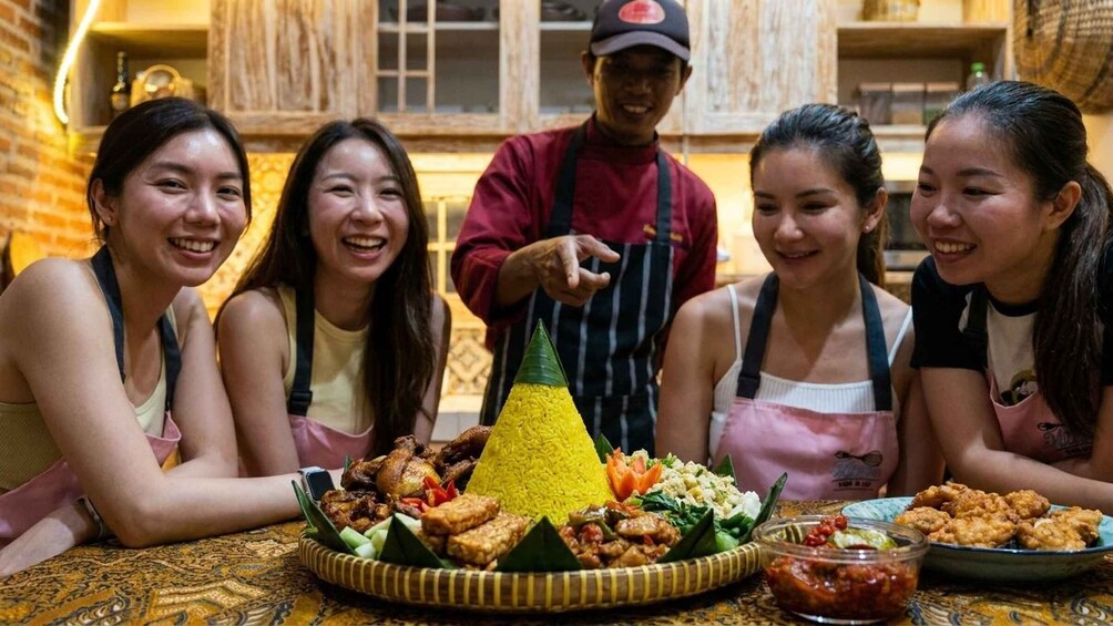 A group of people seated around a table with a variety of dishes, including a yellow rice cone, in a restaurant setting. 5