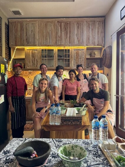 A group of people in a kitchen with wooden cabinets, a tiled backsplash, and a table with water bottles and kitchen utensils. 3