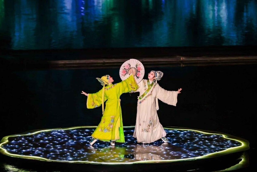 Two performers in traditional costumes on a stage with a reflective surface and a backdrop of vertical lines. 2