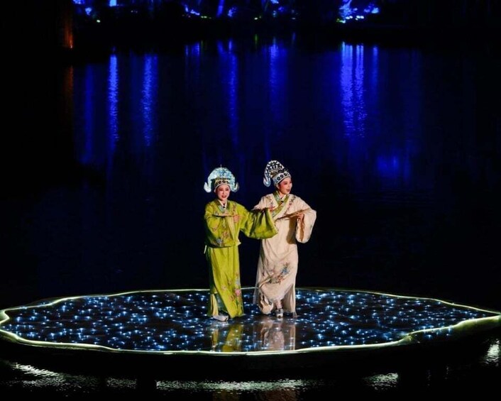 Two performers in traditional costumes on a stage with a water backdrop. 5