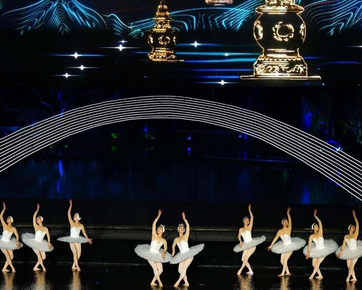 A ballet performance with dancers in white tutus on a stage with a dark background and decorative golden elements. 4