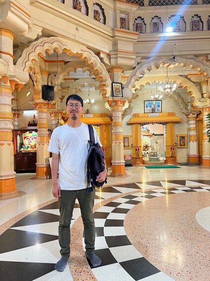 A man standing in a temple with ornate architecture, including carved pillars and arches, and a checkered floor. 4