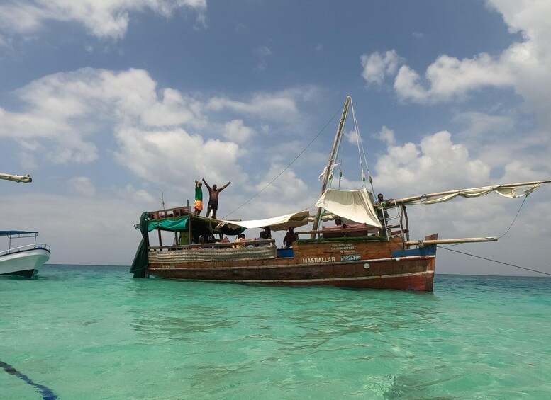 A traditional wooden boat with people on deck, anchored in clear turquoise waters. 1