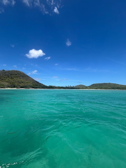 A turquoise sea with a clear sky, distant sandy beaches, and green hills. 3