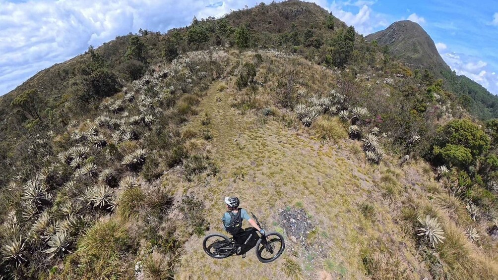 A mountain biker on a trail with sparse vegetation and a mountain in the background. 5
