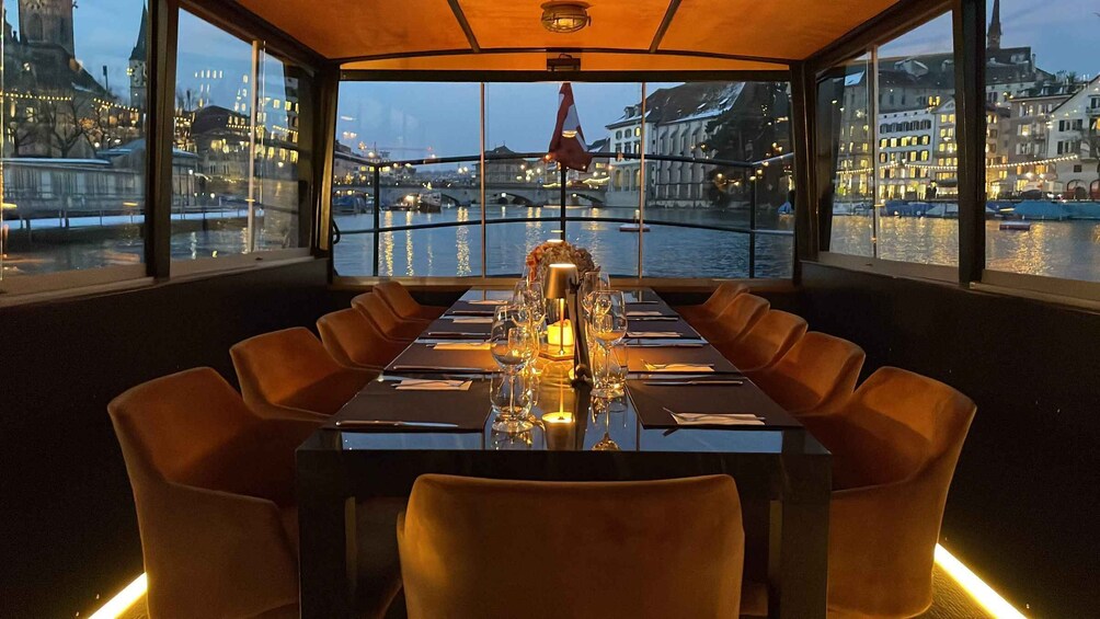 A dining table set for six with a view of a river and cityscape at dusk. 1
