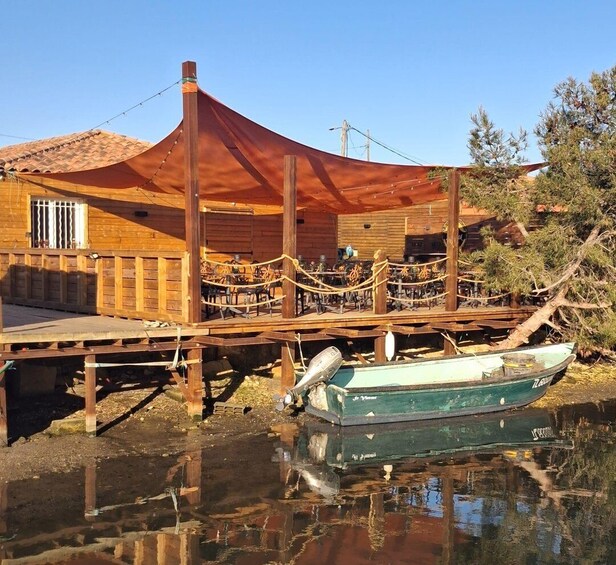 A wooden building with a covered outdoor seating area, a dock, and a small boat. 1