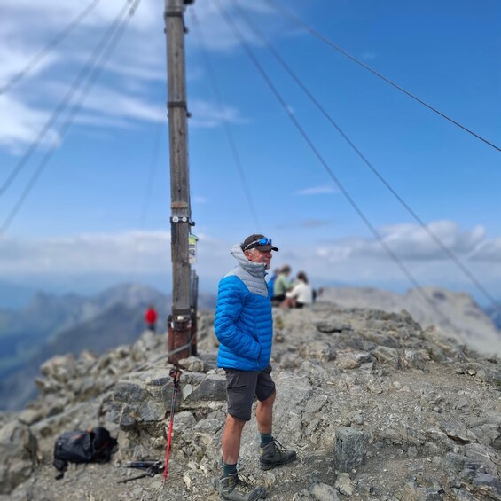 A person standing on a rocky mountain peak with a clear sky and distant mountains. 1