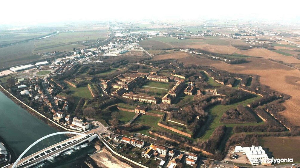 An aerial view of a fortified complex with surrounding fields and a bridge. 1