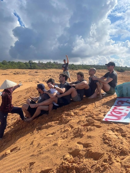 A group of people sitting on a sandy beach with a desert landscape in the background. 4