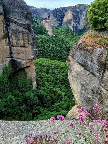 A rocky landscape with a monastery perched atop a cliff, surrounded by dense green forest. 2