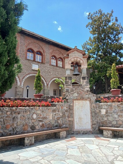 A courtyard with a stone wall, benches, potted plants, and a building with arched windows. 3