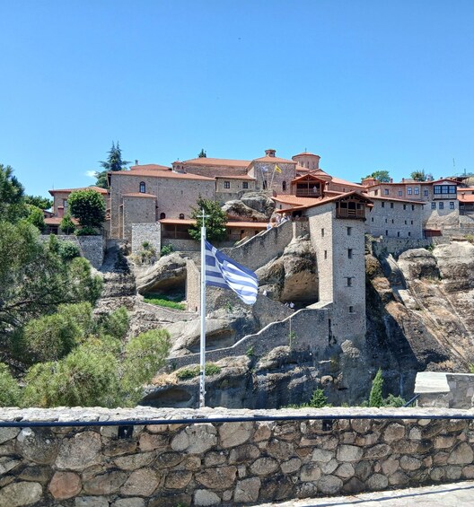 A historic stone fortress with red-tiled roofs, a flagpole with a flag, and a stone wall in the foreground. 4