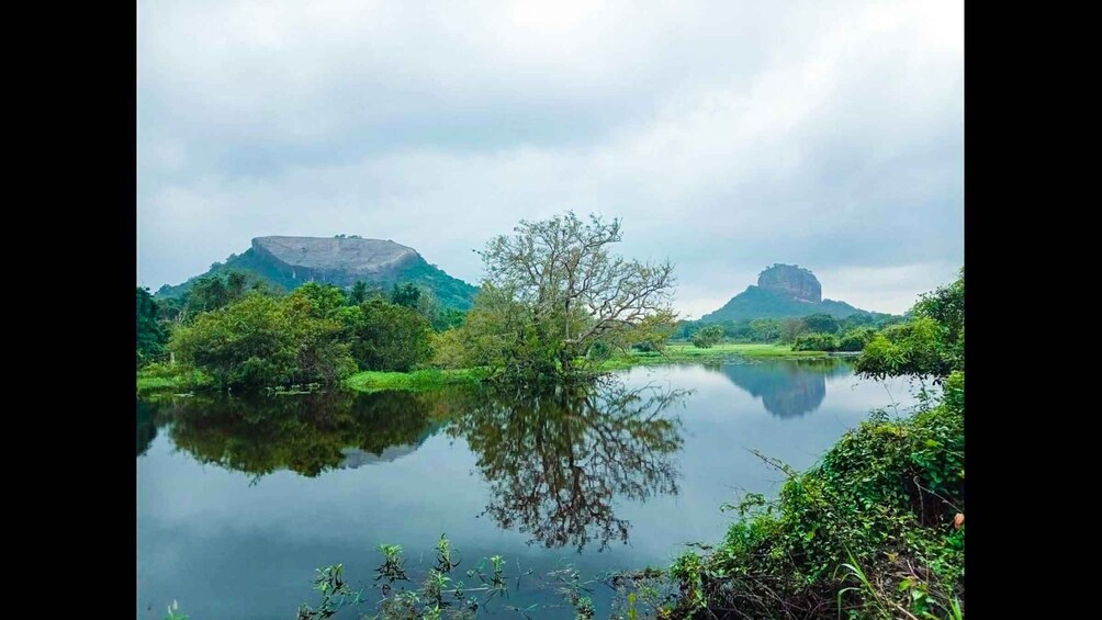 A calm lake reflecting trees and two prominent hills. 4