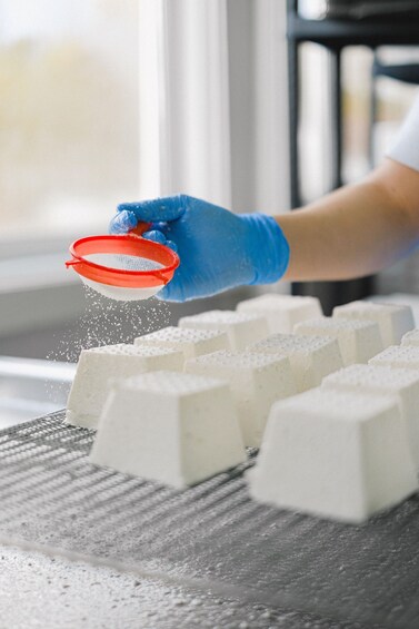 A person in blue gloves handling a red sieve over a tray of white blocks. 1