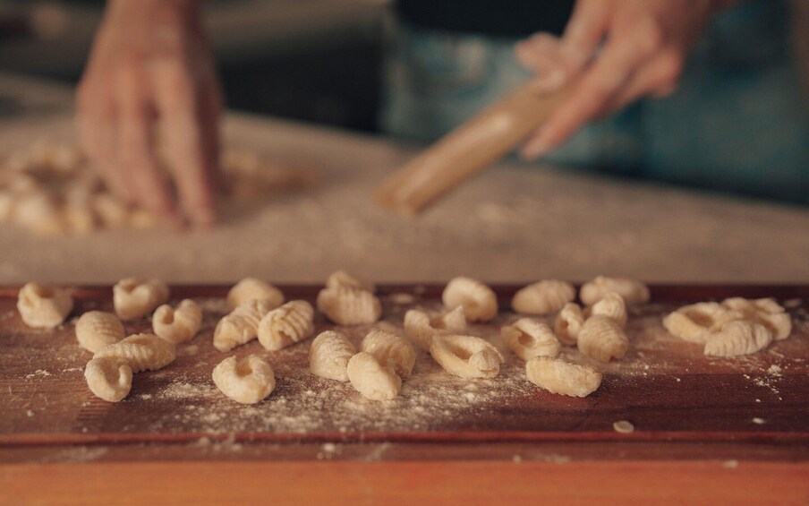 Hands shaping dough on a wooden surface with flour scattered around. 4
