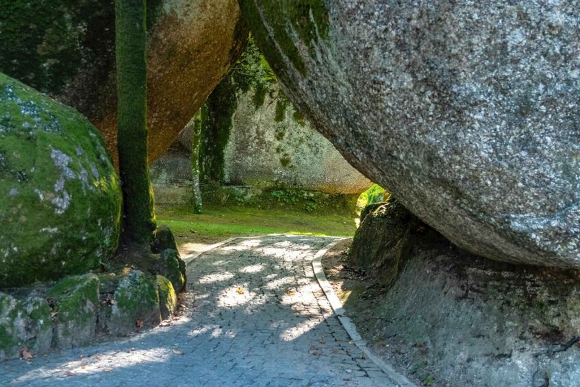 A cobblestone path flanked by large moss-covered rocks in a park. 4
