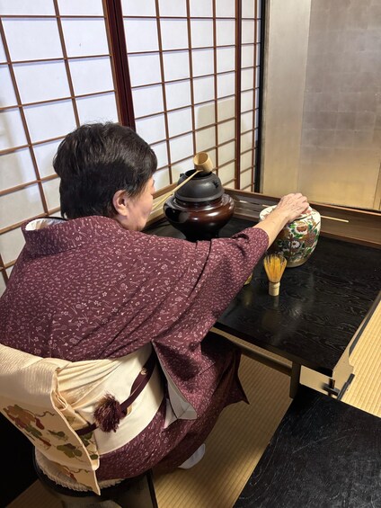 A person sitting at a table with a traditional Japanese tea set, including a tea bowl and a whisk. 2