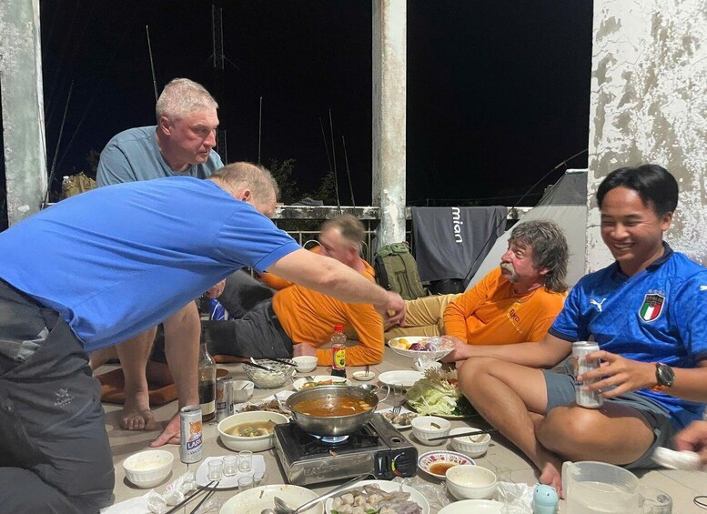 Un grupo de personas reunidas alrededor de una mesa con comida y bebidas, al aire libre de noche. 4