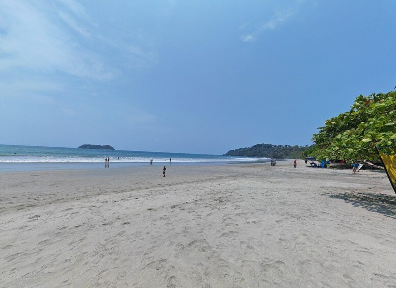 A sandy beach with footprints, a few people, and a distant island. 5