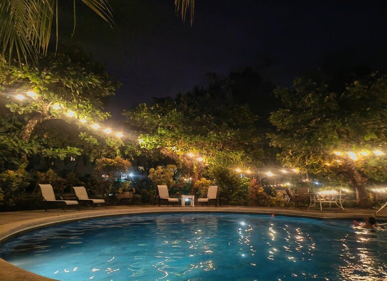 A nighttime swimming pool with string lights and lounge chairs. 4