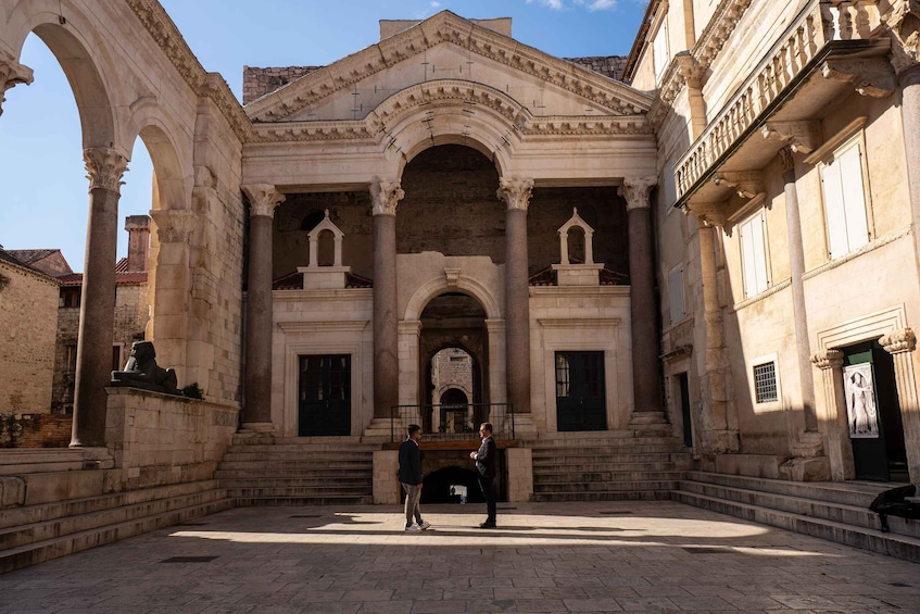 An ancient building with arches and columns, a courtyard, and two people conversing. 4