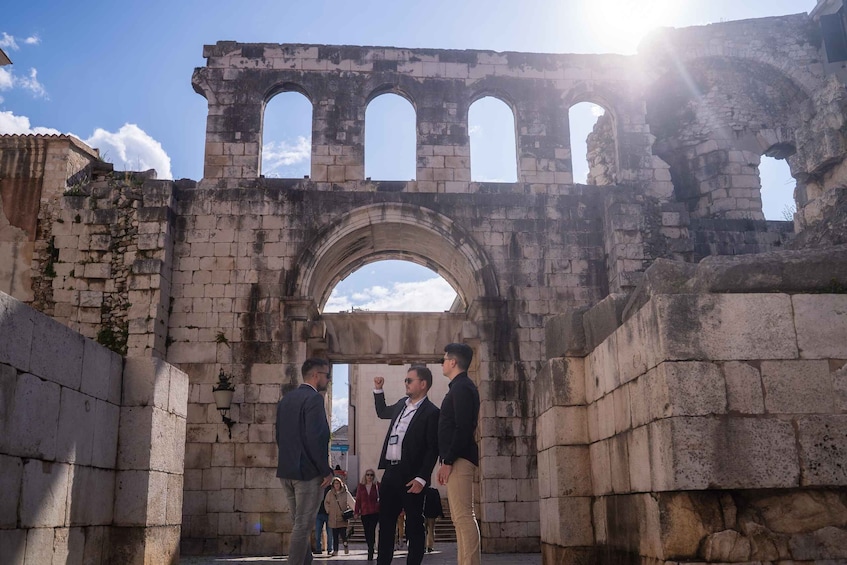 An ancient stone archway with people standing beneath it. 2