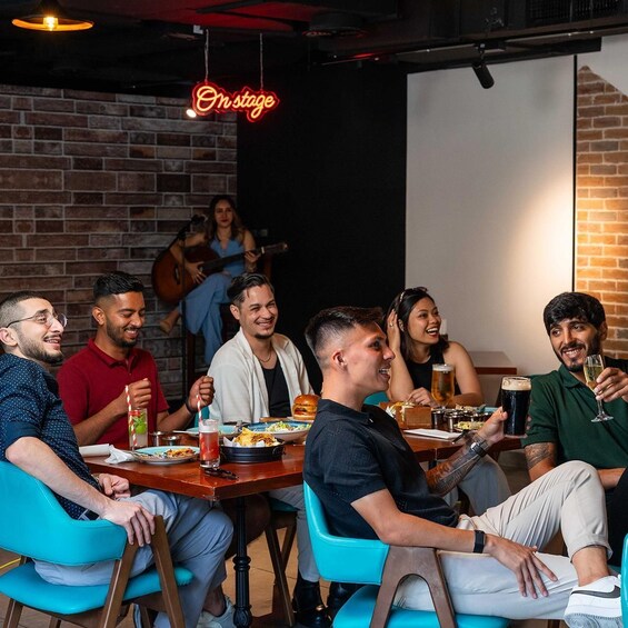 A group of people dining at a restaurant with a brick wall and a neon sign reading 'On Stage.' 3