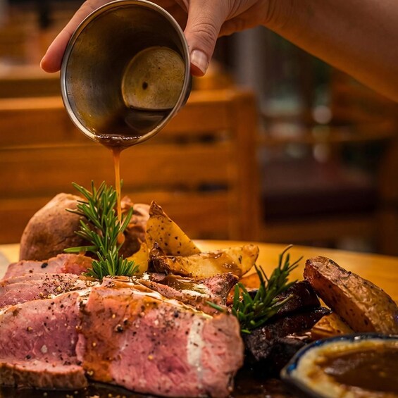 A hand pouring sauce over a steak and potatoes. 1