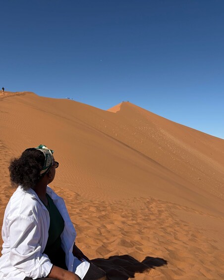 En person sidder på en sanddune under en klar blå himmel. 1