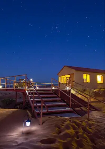 Et strandhus om natten med en trappe til indgangen, en sandet forgrund og en stjerneklar himmel. 2