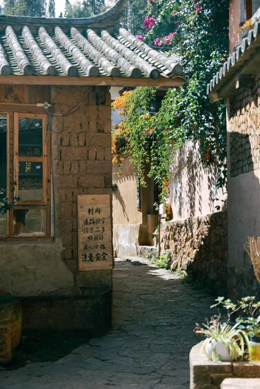 A traditional courtyard with a tiled roof, a stone wall, and a signboard with text. 2