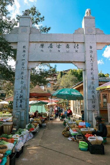 A traditional market entrance with stone archway and Chinese characters, surrounded by vendors and produce. 3