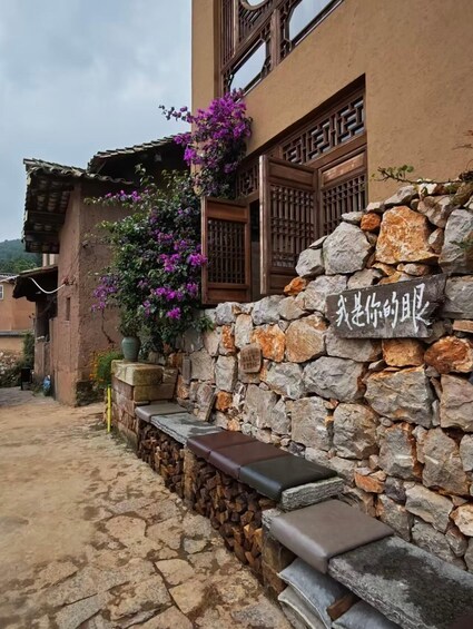 A rustic building with a stone wall, wooden shutters, and purple flowers. 4