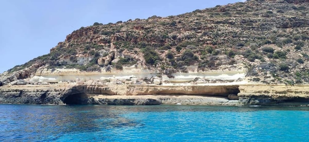 A coastal landscape with a rocky cliff, a clear blue sea, and a natural arch formation. 5