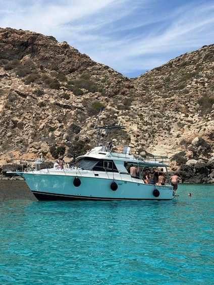 A boat named 'LUNAR CHELSIERE' on clear turquoise water with rocky hills in the background. 2