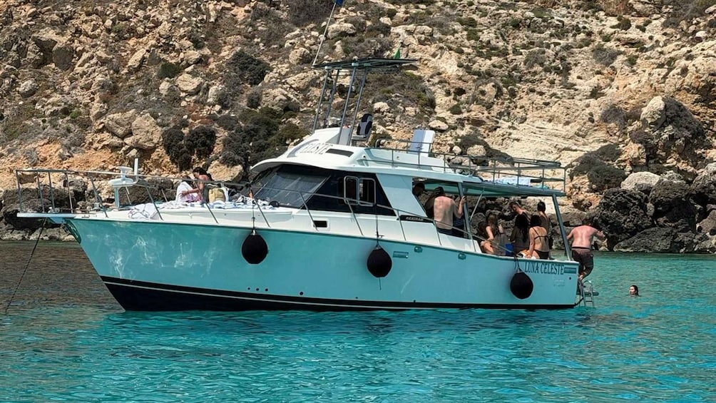 A white boat named 'LUNA CELESTE' with people on board, anchored near rocky cliffs. 1
