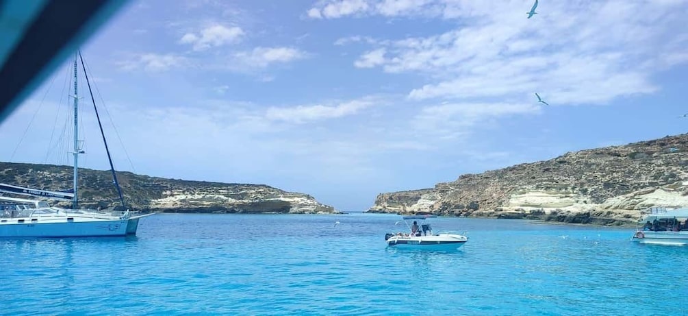 A sailboat and a motorboat in a calm sea with rocky cliffs in the background. 4