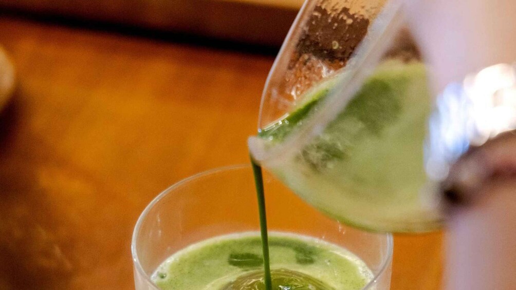 A clear glass being filled with a green liquid. 2
