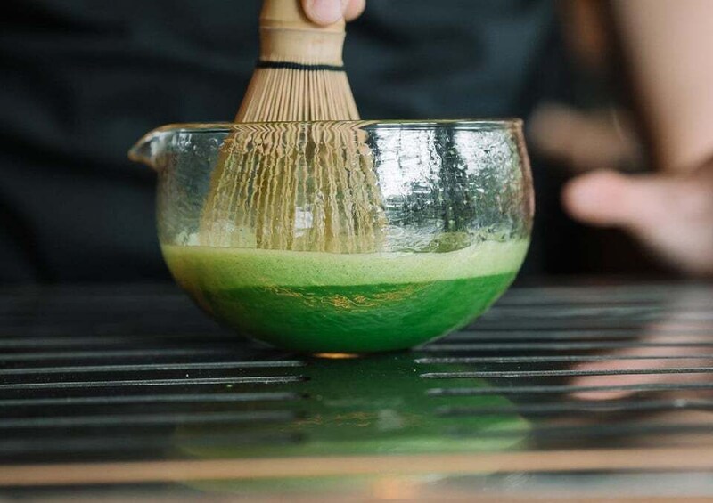 A clear glass bowl with a green substance, a bamboo whisk, and a metal surface. 4