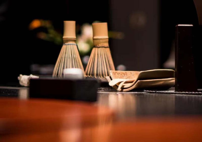A traditional Japanese tea ceremony setting with a tea whisk, a tea bowl, and a dark wooden table. 5