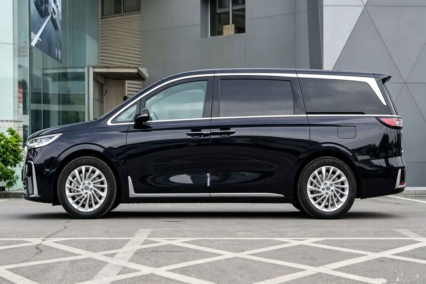 A black minivan parked on a marked parking space in front of a modern building with a geometric facade. 2