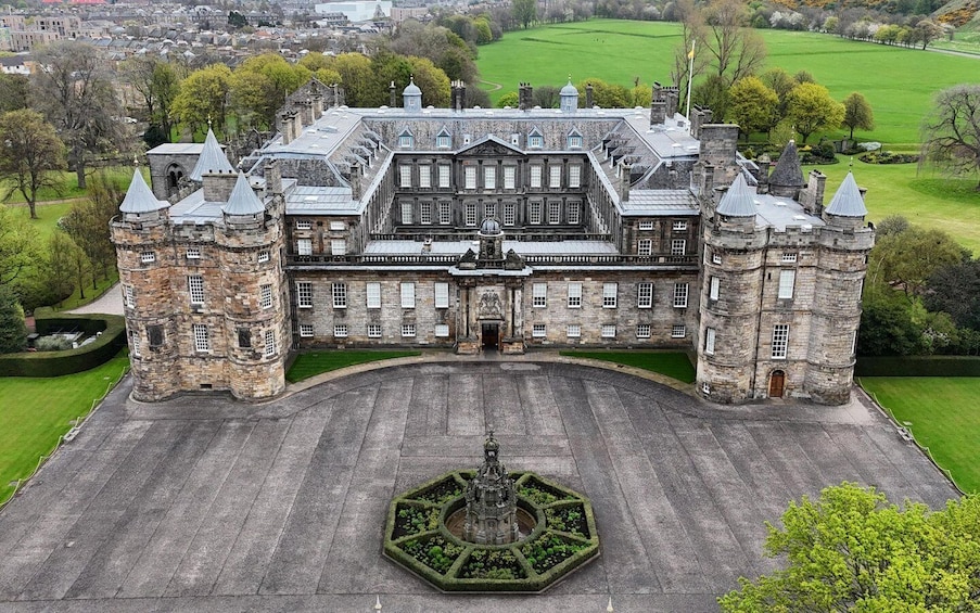 A large stone building with multiple towers and a central entrance, surrounded by well-manicured lawns and a formal garden. 1