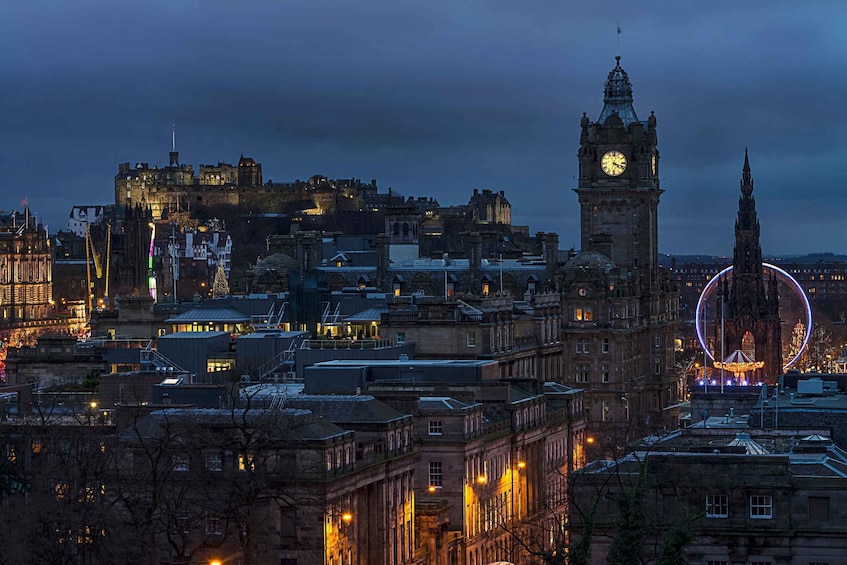 A cityscape at dusk with illuminated buildings, a prominent clock tower, and a castle on a hill. 3