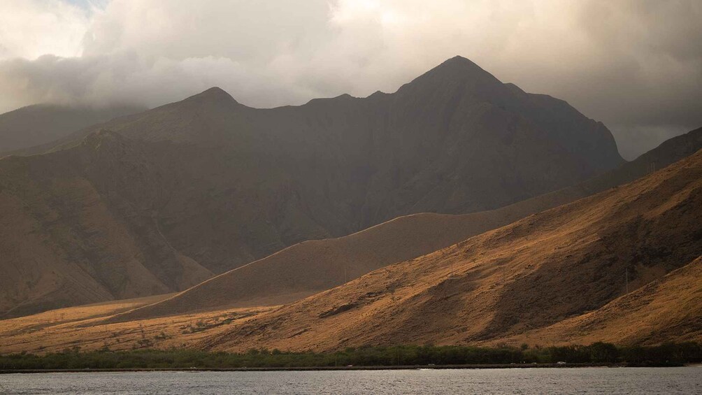 A mountainous landscape with a body of water in the foreground and a cloudy sky above. 3