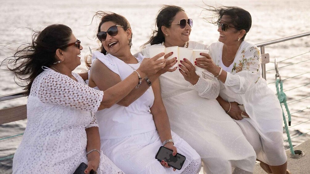 A group of women in white dresses sitting on a dock by the water. 5