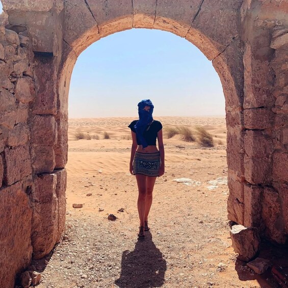 A person standing in an arched doorway with a desert landscape in the background. 1