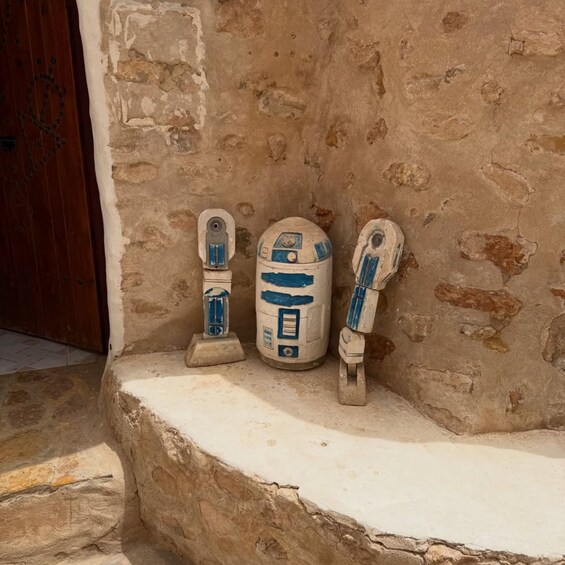 Three R2-D2 figures against a textured wall. 3