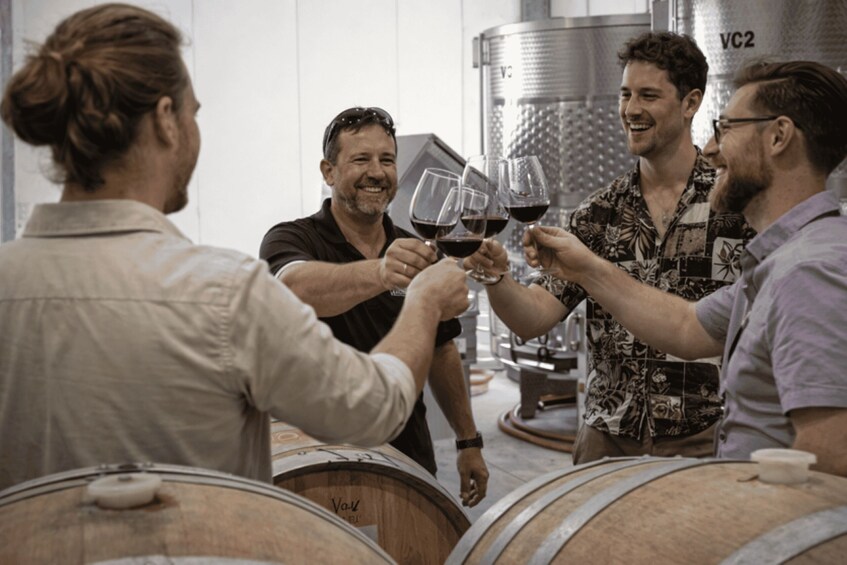 People toasting with wine glasses in a winery setting with barrels and a large tank in the background. 2