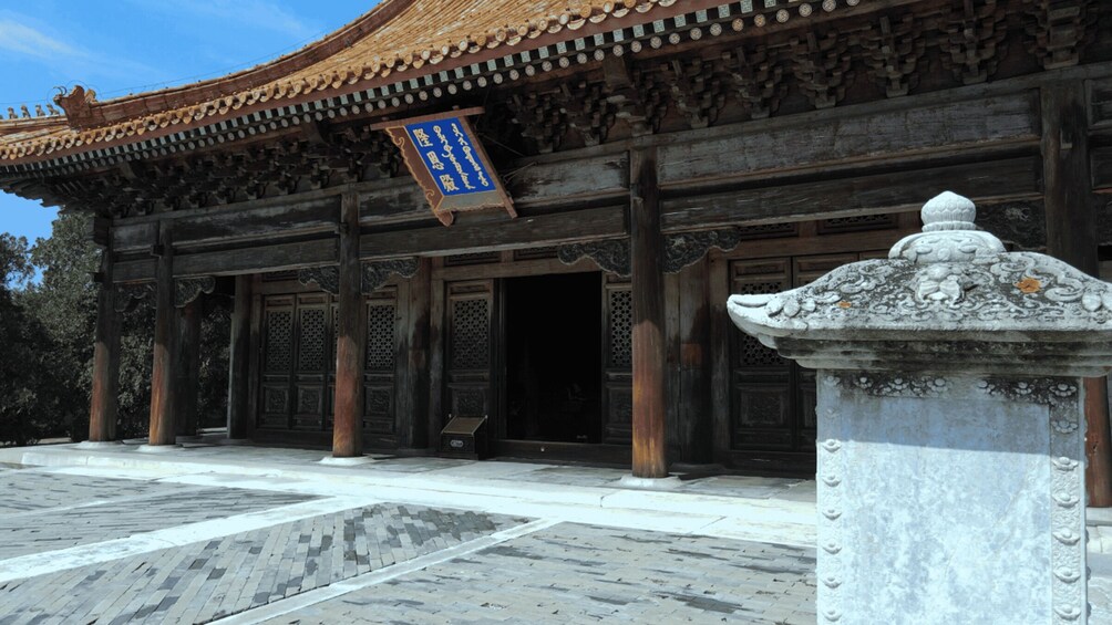 A traditional building with ornate wooden architecture, a stone pedestal, and a blue banner. 5